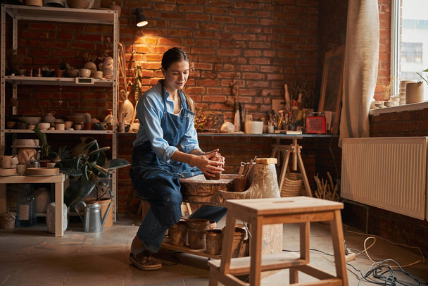 Charming Caucasian craftswoman wearing apron making something on pottery wheel in workshop - Fotoğraf, Görsel