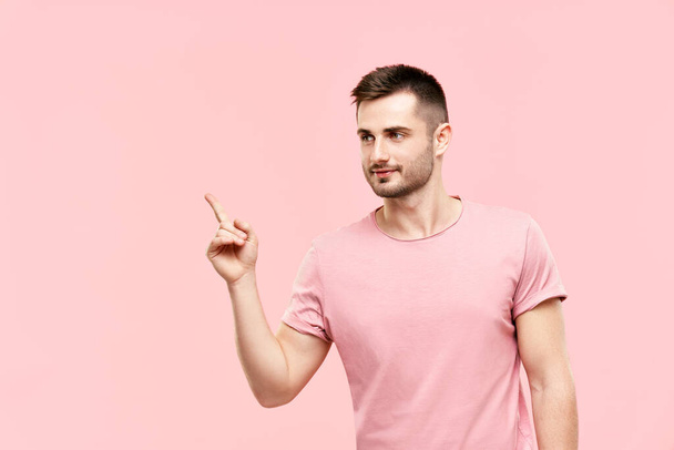 Junger trendiger Mann mit erhobenem Zeigefinger deutet an, Raum isoliert auf rosa Hintergrund zu kopieren - Foto, Bild