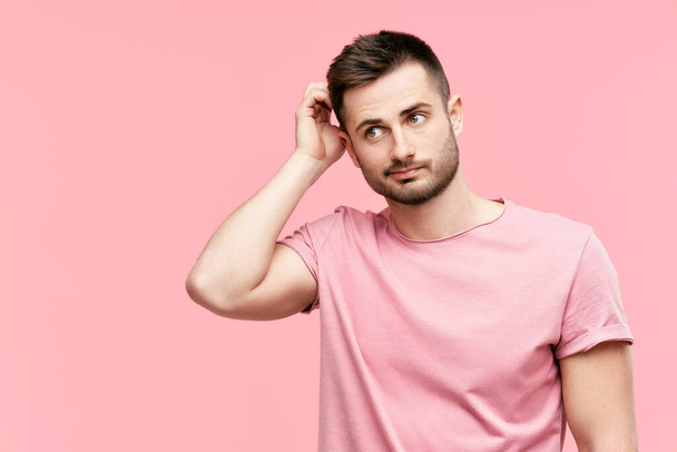 Young pensive man have doubts while scratching head looking to copy space on pink background - Foto, afbeelding