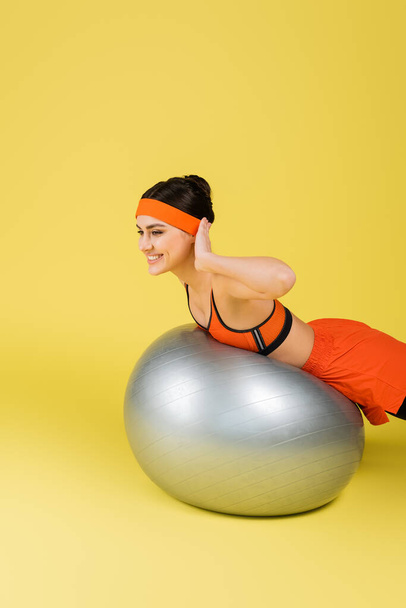smiling sportswoman exercising on fitness ball on yellow background - Foto, immagini