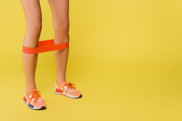 cropped view of sportswoman training with resistance band on legs on yellow background - Φωτογραφία, εικόνα