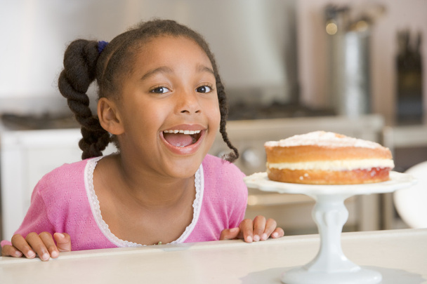 Молодая девушка на кухне смотрит на торт на прилавке улыбаясь
 - Фото, изображение