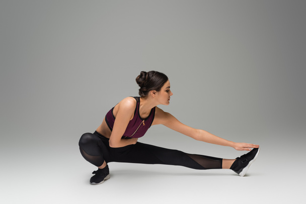 pretty sportswoman stretching on grey background - Photo, image