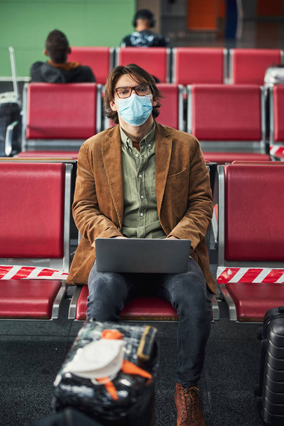 Jovem elegante em máscara médica usando notebook no aeroporto - Foto, Imagem