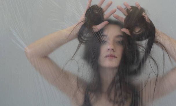 фантастические странные блокировки портрет красивой сексуальной чувственной соблазнительной брюнетки женщина, играя с ее волосами, за завесой прозрачной пластиковой фольги в качестве фона, скопировать пространство - Фото, изображение