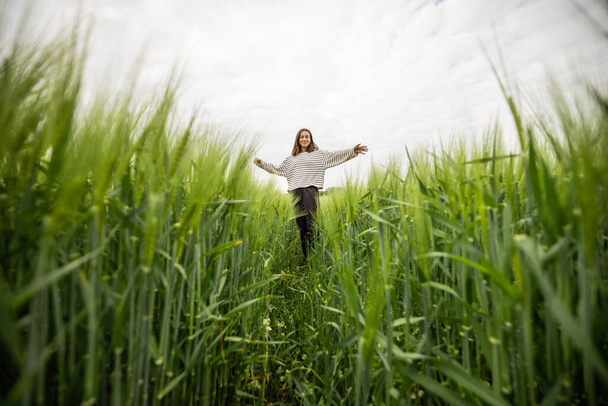 Χαλαρή γυναίκα στέκεται στο πράσινο πεδίο και απολαμβάνει ήρεμη φύση - Φωτογραφία, εικόνα