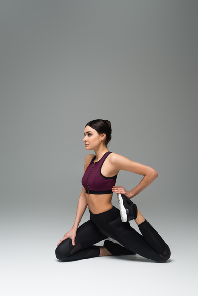 young woman in black sportswear stretching on grey background - Foto, Bild