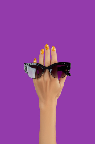 Womans hand holding black sunglasses over purple background - Photo, Image
