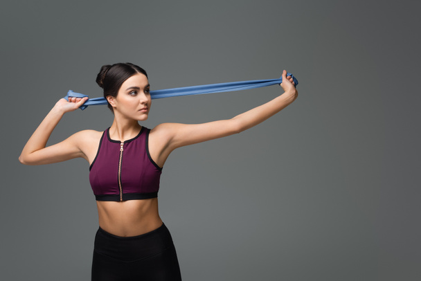 young sportswoman training with resistance band isolated on grey - Fotografie, Obrázek