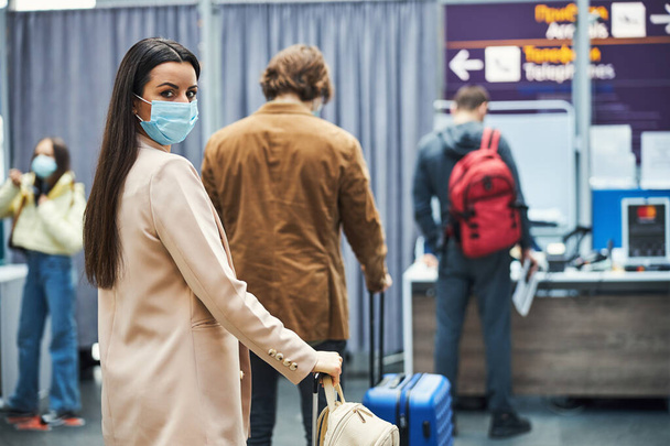 Очаровательная женщина в медицинской маске стоит в очереди в аэропорту - Фото, изображение