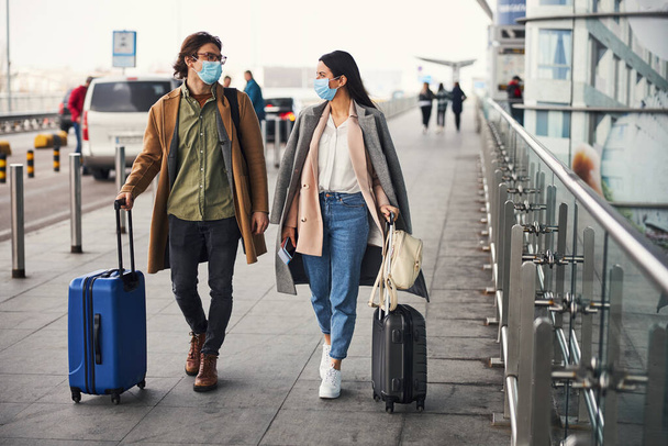 Прекрасна пара в медичних масках, що ходять на відкритому повітрі в аеропорту
 - Фото, зображення