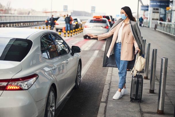Stylish woman in medical mask taking cab at airport - Photo, Image