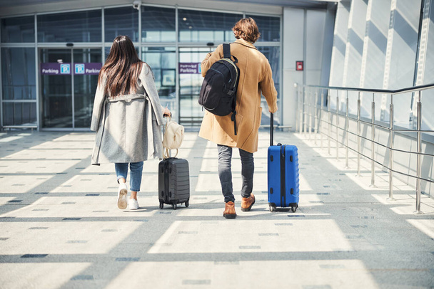 Stylish man and woman carrying travel suitcases at airport - Photo, Image