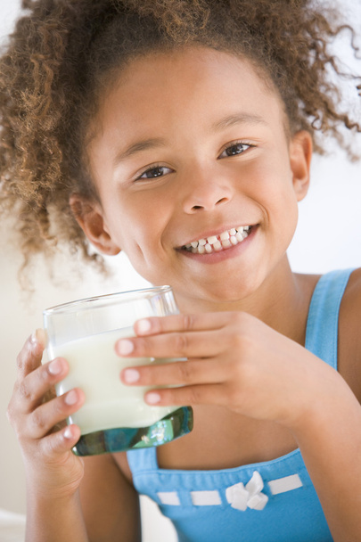 Young girl indoors drinking milk smiling - Valokuva, kuva