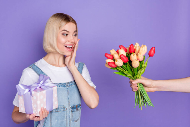 Photo of nice impressed short hairdo blond lady hold flowers present wear white t-shirt isolated on violet background - Photo, Image
