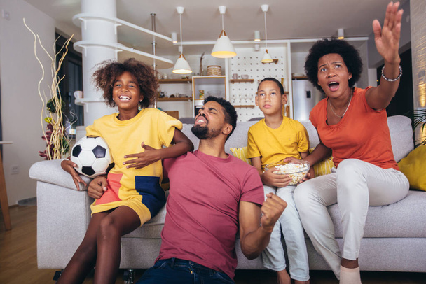 Familia afroamericana feliz viendo el partido de fútbol en la televisión en la sala de estar en casa. - Foto, imagen