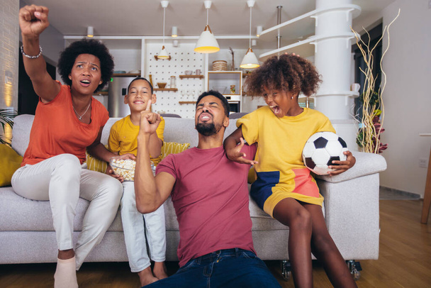 Feliz família afro-americana assistindo jogo de futebol na televisão na sala de estar em casa. - Foto, Imagem
