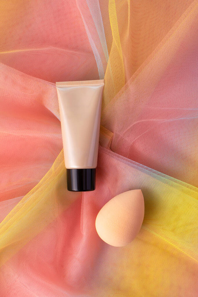 Mockup tonale CC of BB crème foundation make-up en beauty blender spons op kleurrijke regenboog organza stof. Cosmetisch - Foto, afbeelding
