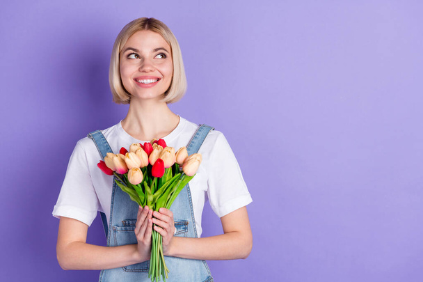 Photo of nice optimistic short hairdo blond lady hold flowers look empty space wear white t-shirt isolated on violet background - Foto, imagen