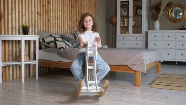 Amazed small preschooler girl rocks on rocking horse by bed - Footage, Video