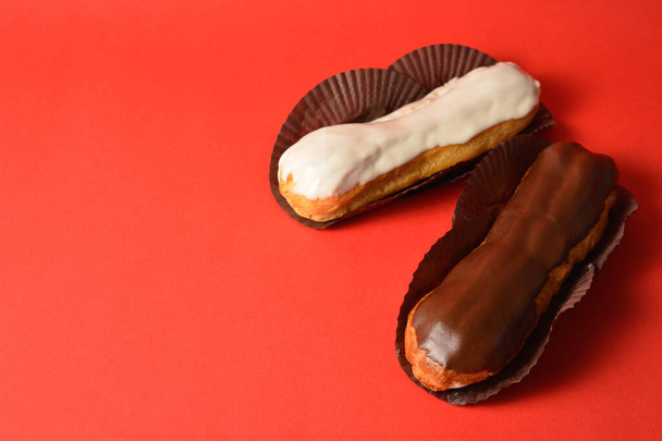 Klassisch französische Desserts. Ein Eclair mit weißer Schokolade darüber und eines mit dunkler Schokolade, gefüllt mit Pudding, serviert auf rotem Hintergrund. Seitenansicht. Leerzeichen kopieren - Foto, Bild