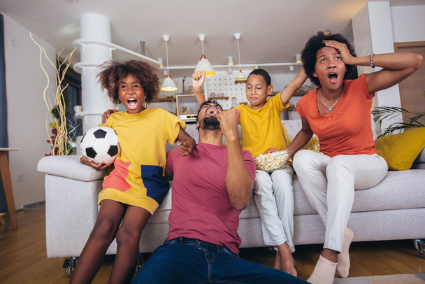 Boldog afro-amerikai család focimeccset néz a tévében otthon, a nappaliban.. - Fotó, kép
