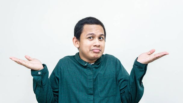 Portret bezmyślnego Azjaty Malajczyka śmiesznie uśmiechającego się w zielonej koszuli, wzruszającego rękami z różnych stron, uśmiechającego się i nieświadomego tego, co dzieje się na białym tle. - Zdjęcie, obraz