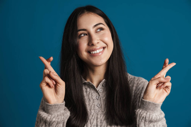 Smiling woman with fingers crossed gesture isolated on a blue background - Foto, afbeelding
