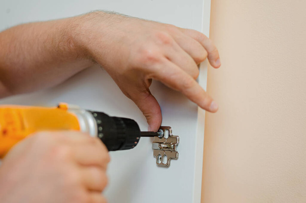 um homem aperta um parafuso com uma chave de fenda em uma dobradiça da porta em uma porta branca do armário - Foto, Imagem