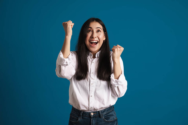 Exited asian girl making winner gesture and screaming isolated over blue background - Foto, Imagem
