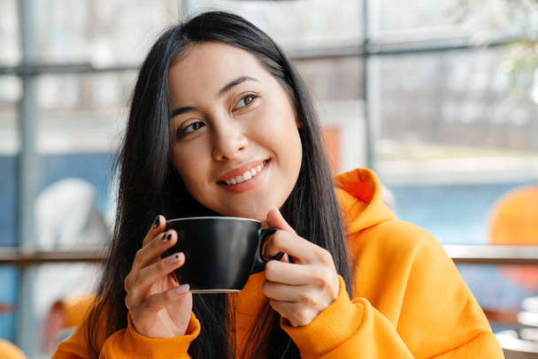 Young asian woman smiling while drinking coffee in cafe - Fotografie, Obrázek