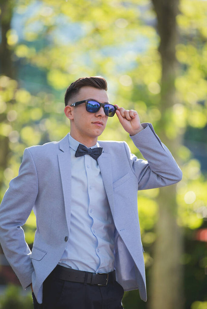 The portrait of a confident stylish man in a suit touching his sunglasses - Фото, изображение