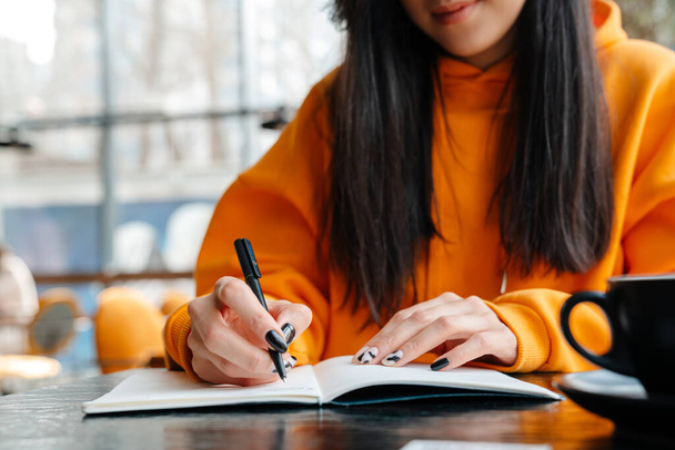 Pleased asian woman writing down notes while sitting in cafe - Photo, image