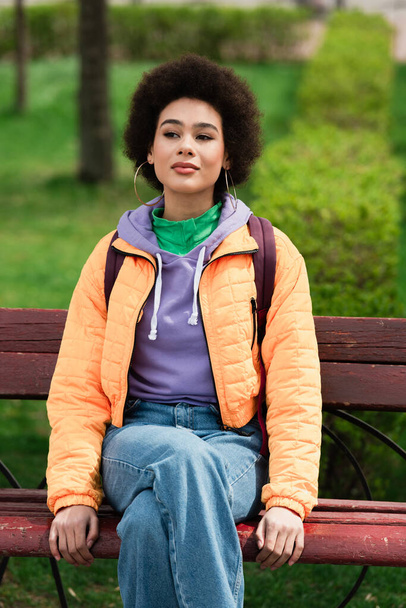 Mujer afroamericana bastante sentada en el banco al aire libre  - Foto, Imagen
