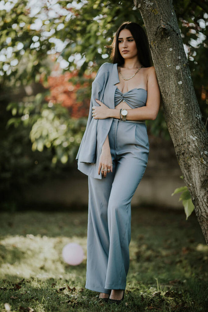 A vertical shot of a young female in a sexy gray pantsuit posing outdoors - Φωτογραφία, εικόνα