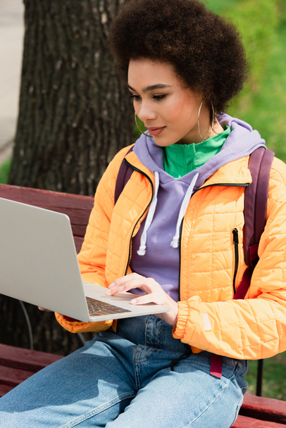 African american freelancer using laptop on bench outdoors  - Photo, Image