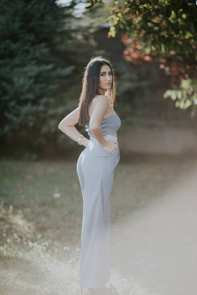 A vertical shot of a young female in a sexy gray pantsuit posing outdoors - Zdjęcie, obraz