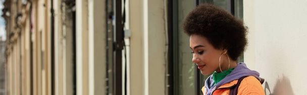 Sonriente mujer afroamericana de pie cerca del edificio, pancarta  - Foto, imagen