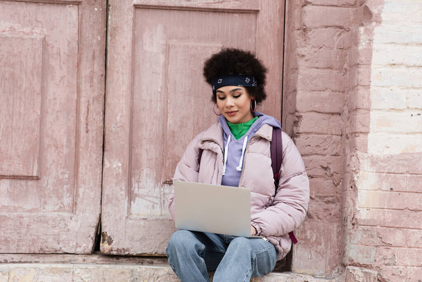African american freelancer in jacket using laptop near building  - Fotó, kép