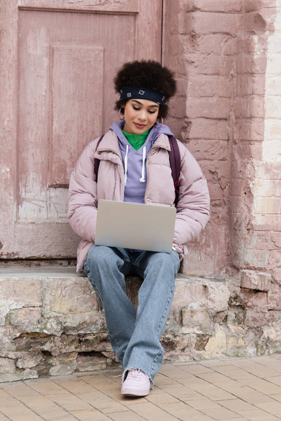 Trendi afro-amerikai nő használja laptop a lépcsőn közel épület  - Fotó, kép