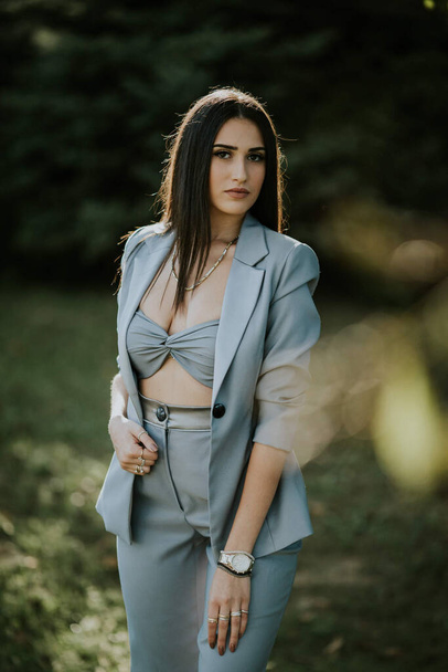 A vertical shot of a young female in a sexy gray pantsuit posing outdoors - Fotografie, Obrázek