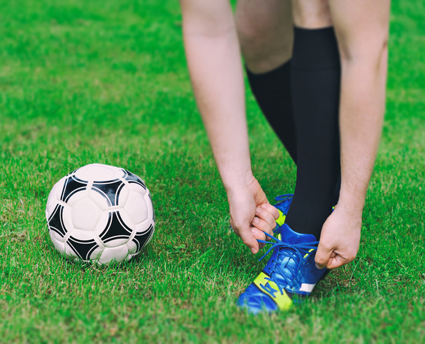 Jugador de fútbol atándose los zapatos en el campo
. - Foto, imagen