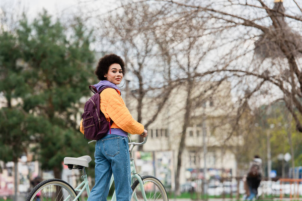 African american woman in jacket standing near bike outdoors  - Фото, зображення