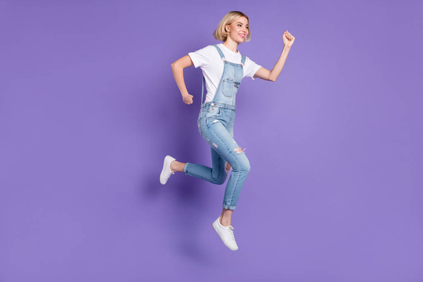 Full size profile photo of nice optimistic short hairdo blond lady run wear white t-shirt overall isolated on violet background - Фото, изображение