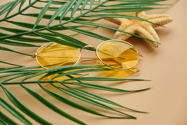 Close up Yellow Sunglasses and palm leaves top view on beige background with copy space. summer vacation background - Photo, Image
