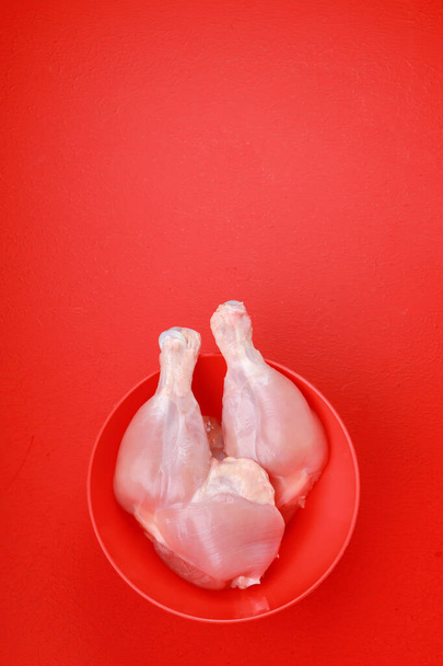 Rohe Hühnerkeulen oder -schenkel ohne Haut in einer roten Schüssel auf rotem einfarbigem Hintergrund angeordnet - Foto, Bild