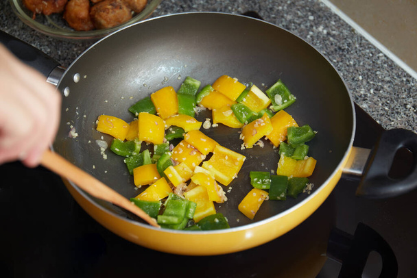 Um shot close-up de pimentas amarelas e verdes sendo cozidas em uma frigideira - Foto, Imagem