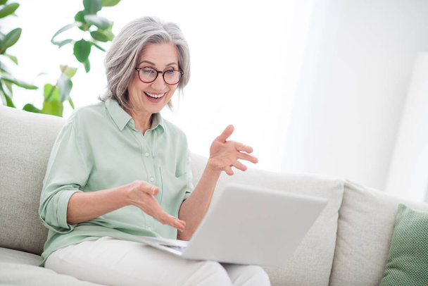 Photo of positive aged person sit on couch look laptop speak tell have good mood free time indoors - Фото, зображення