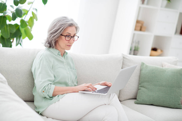 Photo of charming aged woman sit on couch look hold use laptop typing email free time vacation indoors - Fotoğraf, Görsel