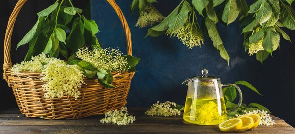 Травяной чай здоровья старшего цветка окружает свежие цветы и листья в корзине, темный деревенский стиль. Закрыть. - Фото, изображение